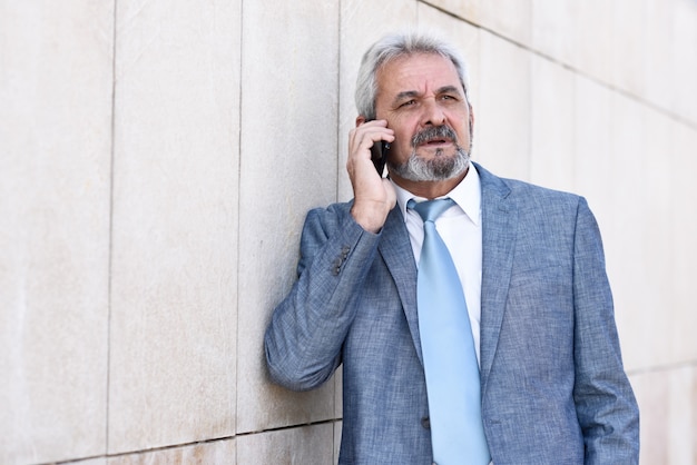 Empresário sênior com smartphone fora do prédio de escritórios moderno.