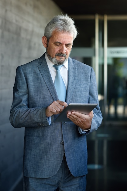 Empresário sênior com tablet computador fora do prédio de escritórios moderno.