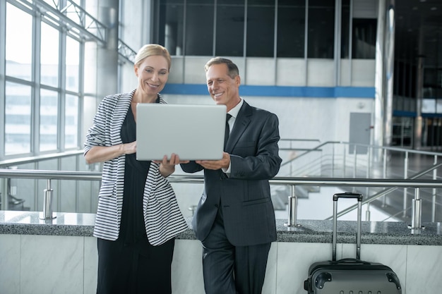 Empresário sorridente e uma senhora de negócios satisfeita usando o notebook no terminal do aeroporto