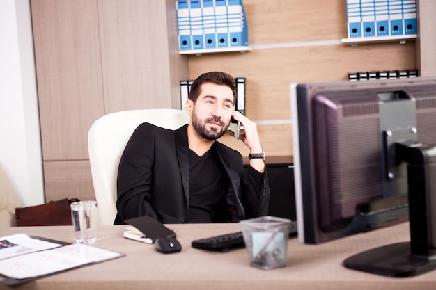 Empresário sorridente falando ao telefone enquanto trabalhava em seu escritório. empresário em ambiente profissional