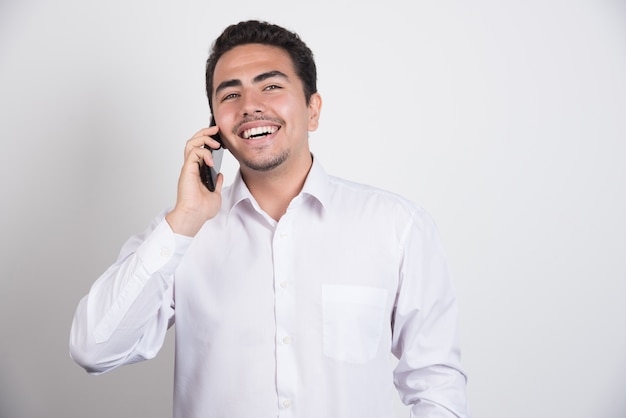 Empresário sorridente, falando com o telefone em fundo branco.