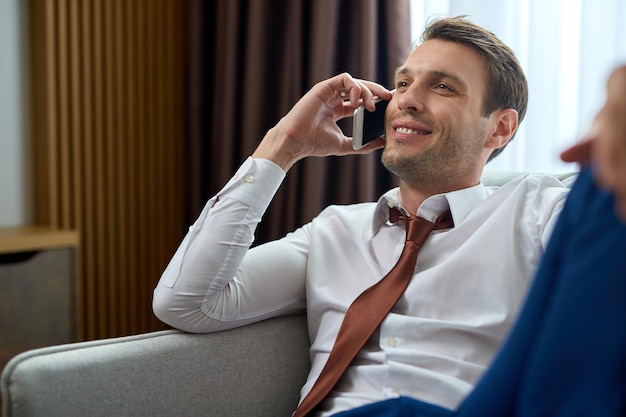 Empresário sorridente relaxando em um quarto de hotel e se comunicando por telefone celular