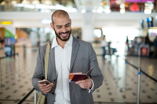 Empresário sorridente segurando um cartão de embarque e verificando o celular