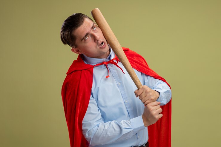 Foto grátis empresário super-herói com capa vermelha se socando com taco de beisebol em pé sobre um fundo claro