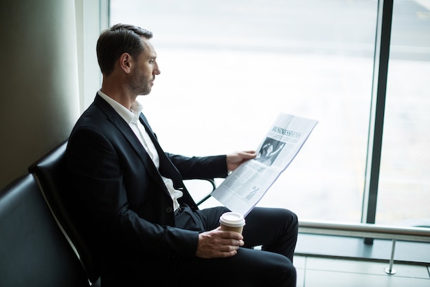 Empresário tomando café enquanto lê o jornal na sala de espera