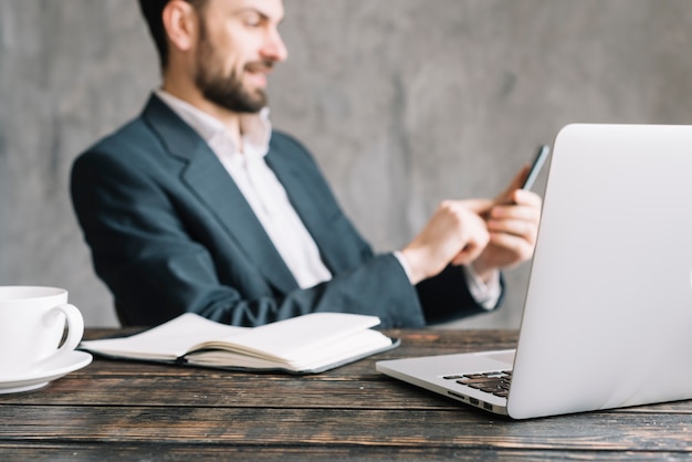 Empresário turva navegando smartphone perto de laptop