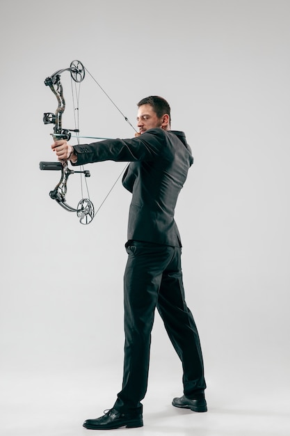 Foto grátis empresário visando o alvo com arco e flecha, isolado no fundo cinza do estúdio.