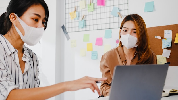 Empresários da Ásia usando apresentação de computador, reunião de brainstorming sobre novos colegas de projeto e usam máscara protetora no novo escritório normal.