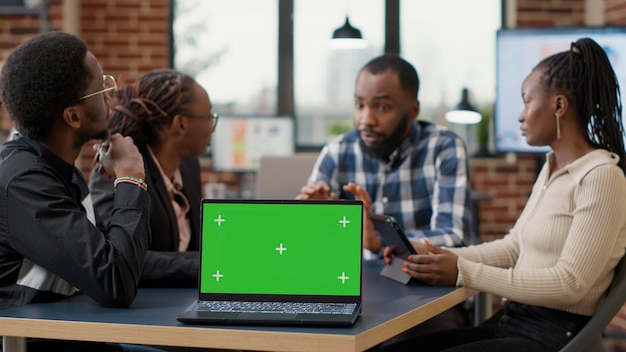 Empresários participando de reunião de briefing com tela verde no laptop, usando espaço de cópia em branco com fundo de croma isolado e modelo de maquete. tecnologia moderna no escritório de inicialização.