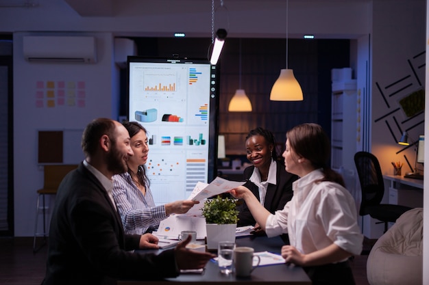 Empresários workaholics debatendo ideias para empresas financeiras, analisando papelada de estratégia tarde da noite na sala de reuniões do escritório de negócios