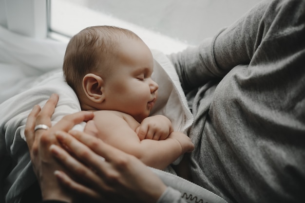 Encantador menino recém-nascido dorme nos braços da mãe