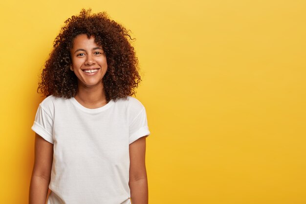 Encantadora adolescente de pele escura com cabelo afro crespo, expressa alegria e bom humor