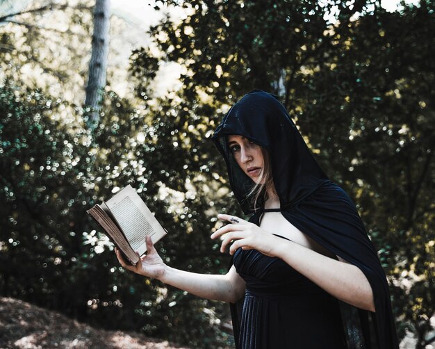Encantadora com livro de feitiços na floresta ensolarada