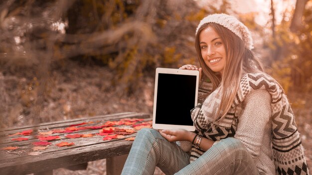 Encantadora dama mostrando tablet perto de mesa no parque