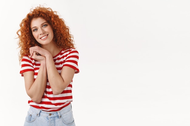 Foto grátis encantadora, gentil, ruiva, cacheada, 25 anos, olhos azuis, pressione as palmas das mãos no peito, doce cena adorável sorrindo agradecido inclinando a cabeça apreciar presente incrível, parede branca