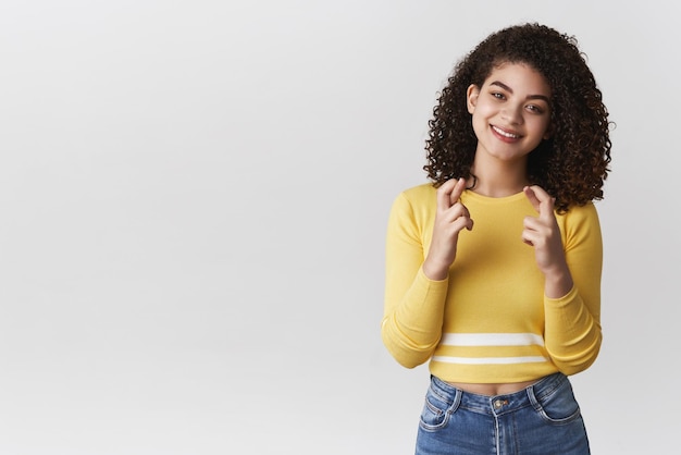 Encantadora jovem esperançosa e tenra sorrindo dedos cruzados boa sorte fazendo desejo sorrindo alegremente fazendo desejo sonhando desejo se realizando fundo branco em pé fundo branco fiel