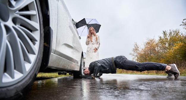 Foto grátis encantadora jovem observando como o homem consertando a roda do carro