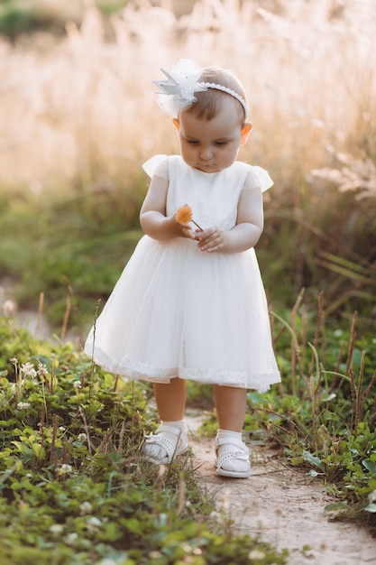 Encantadora menina de vestido branco caminha ao longo do caminho no campo