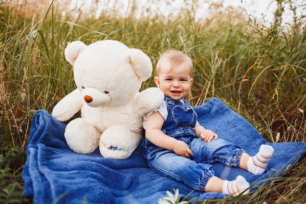 Foto grátis encantadora menina senta-se com um grande urso branco de brinquedo no campo