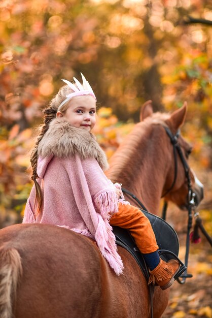 Encantadora menina vestida como uma princesa passeios a cavalo ao redor da floresta de outono
