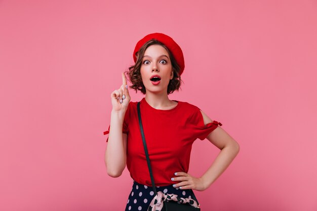 Encantadora modelo francesa de cabelos curtos, posando com roupas vermelhas. Foto interna de mulher branca interessada na boina isolada.