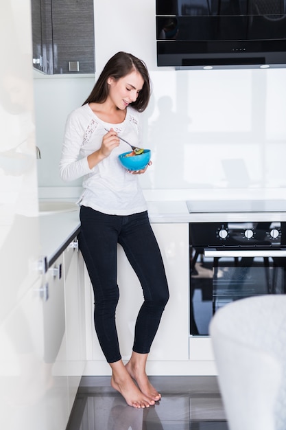 Encantadora mulher jovem comendo salada na cozinha