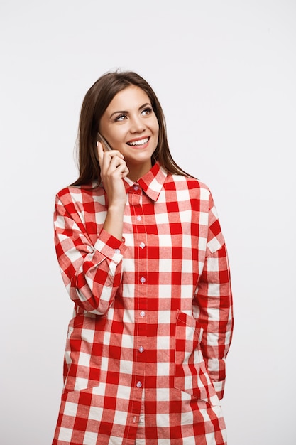 Encantadora mulher jovem em camisa de seleção longa na moda fazendo chamadas telefônicas