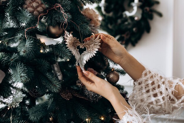 Encantadora mulher loira de vestido branco coloca em uma sala com grande árvore de Natal