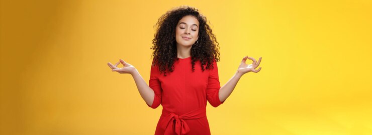 Foto grátis encantadora mulher sonhadora e feliz pacífica em vestido vermelho com cabelo encaracolado em posição de lótus com mu
