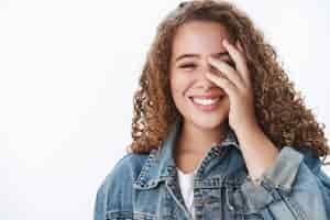 Foto grátis encantadora otimista otimista sonhadora garota gorda de cabelos cacheados sorrindo dentes brancos corando sedutor esconder metade do rosto palma divirta-se rindo fofa, parede do estúdio