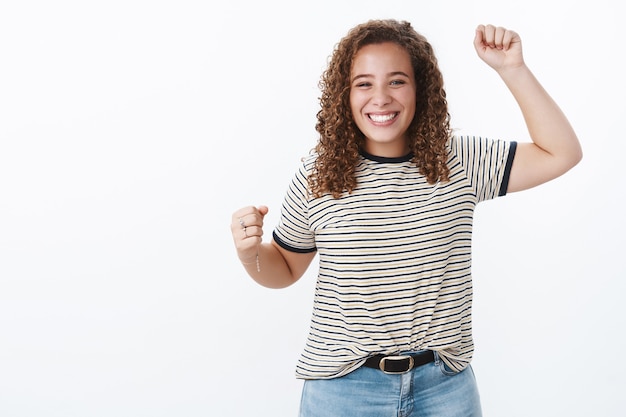 Foto grátis encantadora, triunfante, alegre, simpática, jovem, de cabelo encaracolado, corpo positivo, sorrindo, realizando aumento de metas, cabe gesto de vitória receber prêmio de troféu