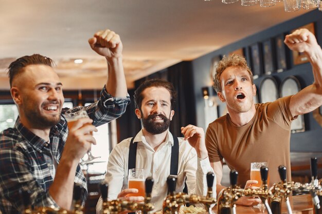 Encontro com os melhores amigos. Três jovens felizes no casual wear conversando e bebendo cerveja enquanto estão sentados juntos no bar.