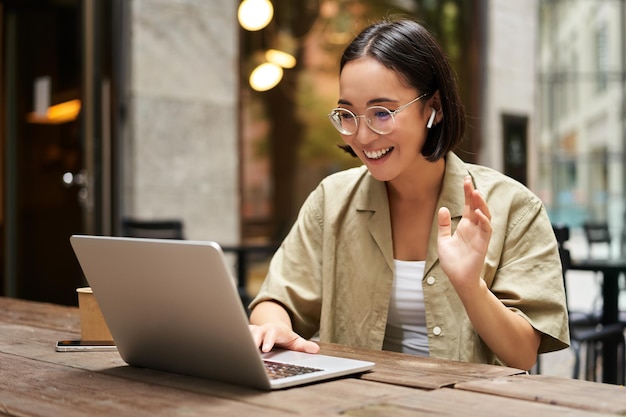 Foto grátis encontro on-line com uma jovem mulher asiática urbana falando com um bate-papo por vídeo de laptop gesticulando sentado em um o