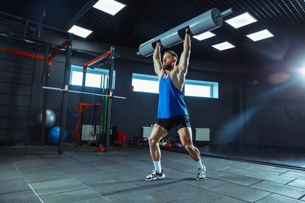 Energia selvagem. Jovem atleta caucasiano musculoso treinando na academia, fazendo exercícios de força, praticando, trabalhando na parte superior do corpo com pesos e halteres. Fitness, wellness, conceito de estilo de vida saudável.