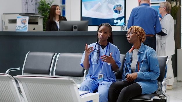 Enfermeira afro-americana e paciente usando holograma médico para analisar a projeção holográfica do metaverso AI na sala de espera. Pessoas olhando para a realidade aumentada da inteligência artificial. Tiro de tripé.