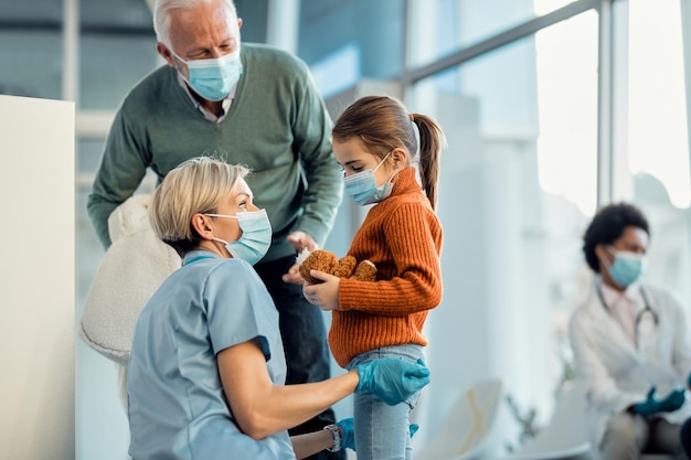 Enfermeira carinhosa conversando com uma garotinha triste que veio para consulta médica com seu avô