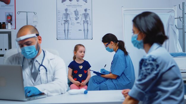 Enfermeira com máscara de proteção escrevendo dados da criança na área de transferência durante covid-19. Médico especialista em medicina que presta consultoria, tratamento, exame em gabinete de hospital.