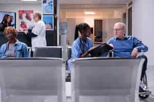 Foto grátis enfermeira conversando com paciente idoso com deficiência crônica, sentado em cadeira de rodas na área de espera. assistente médico que consulta o homem com deficiência física, dando tratamento para recuperação.