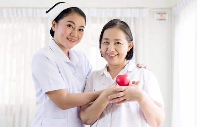 Enfermeira e idosa segurando modelo de coração vermelho nas mãos juntasdia internacional das enfermeiras Foto Premium