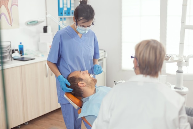 Enfermeira médica que faz a limpeza profissional dos dentes para o paciente durante a consulta ortodôntica no consultório de estomatologia. equipe do hospital examinando dor de dente preparando o tratamento dentário