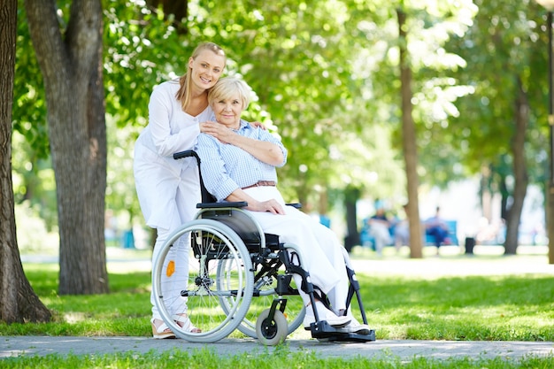Enfermeira que abraça a mulher idosa na cadeira de rodas