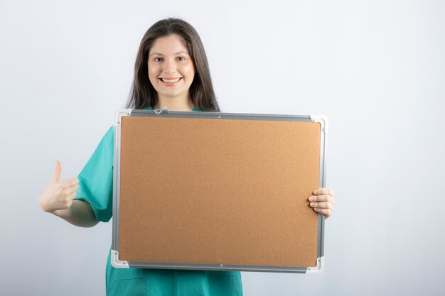Enfermeira sorridente segurando a placa e apontando o polegar para cima.