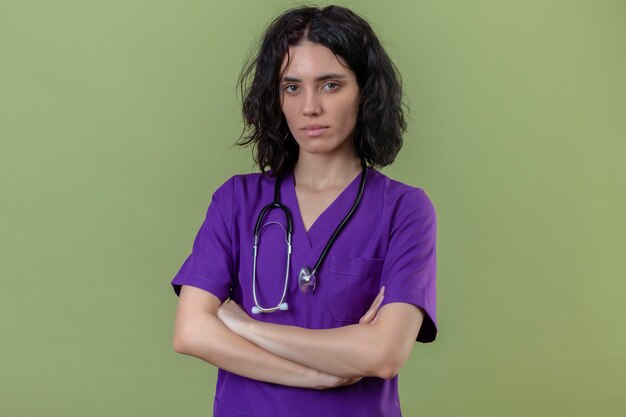 enfermeira vestindo uniforme e estetoscópio em pé com os braços cruzados e o rosto carrancudo no verde isolado