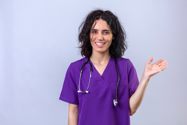 enfermeira vestindo uniforme e estetoscópio em pé com uma cara feliz e um sorriso confiante apresentando com a mão em branco