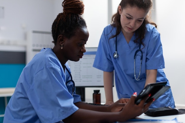 Enfermeiras médicas analisando os sintomas da doença, discutindo o tratamento de saúde, trabalhando no escritório do hospital. Trabalho em equipe verificando medicamentos farmacêuticos em um computador tablet sentado na mesa