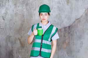 Foto grátis engenheira com capacete verde segurando uma caneca de café verde