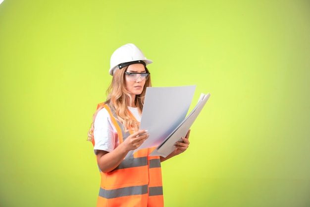 Engenheira de capacete e equipamento, segurando o plano de projeto e corrigindo-o.