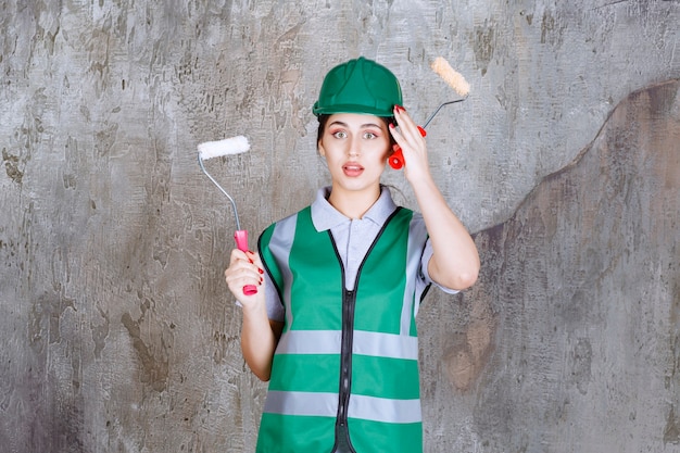 Engenheira de capacete verde segurando um rolo aparador para pintura de parede e pensando em novos métodos