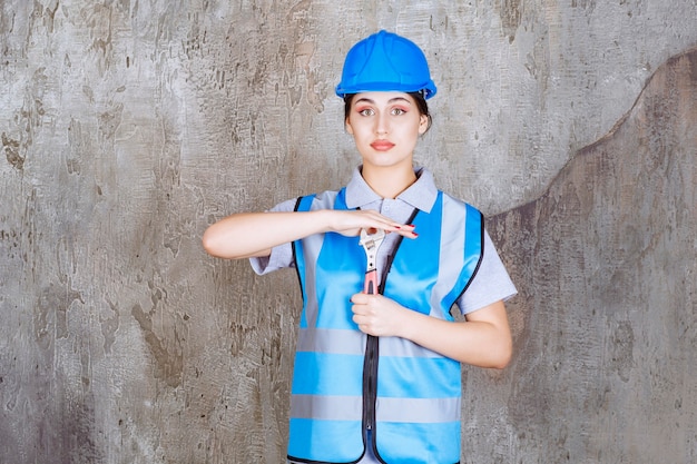 Foto grátis engenheira de uniforme azul e capacete segurando uma chave metálica