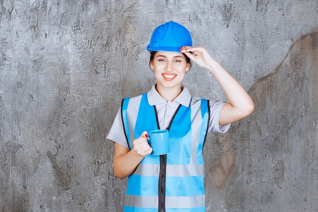 Engenheira de uniforme azul e capacete segurando uma xícara de chá azul